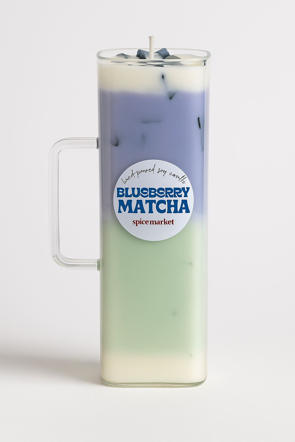 Candle in a glass mug with blueberry matcha flavor label on a white background
